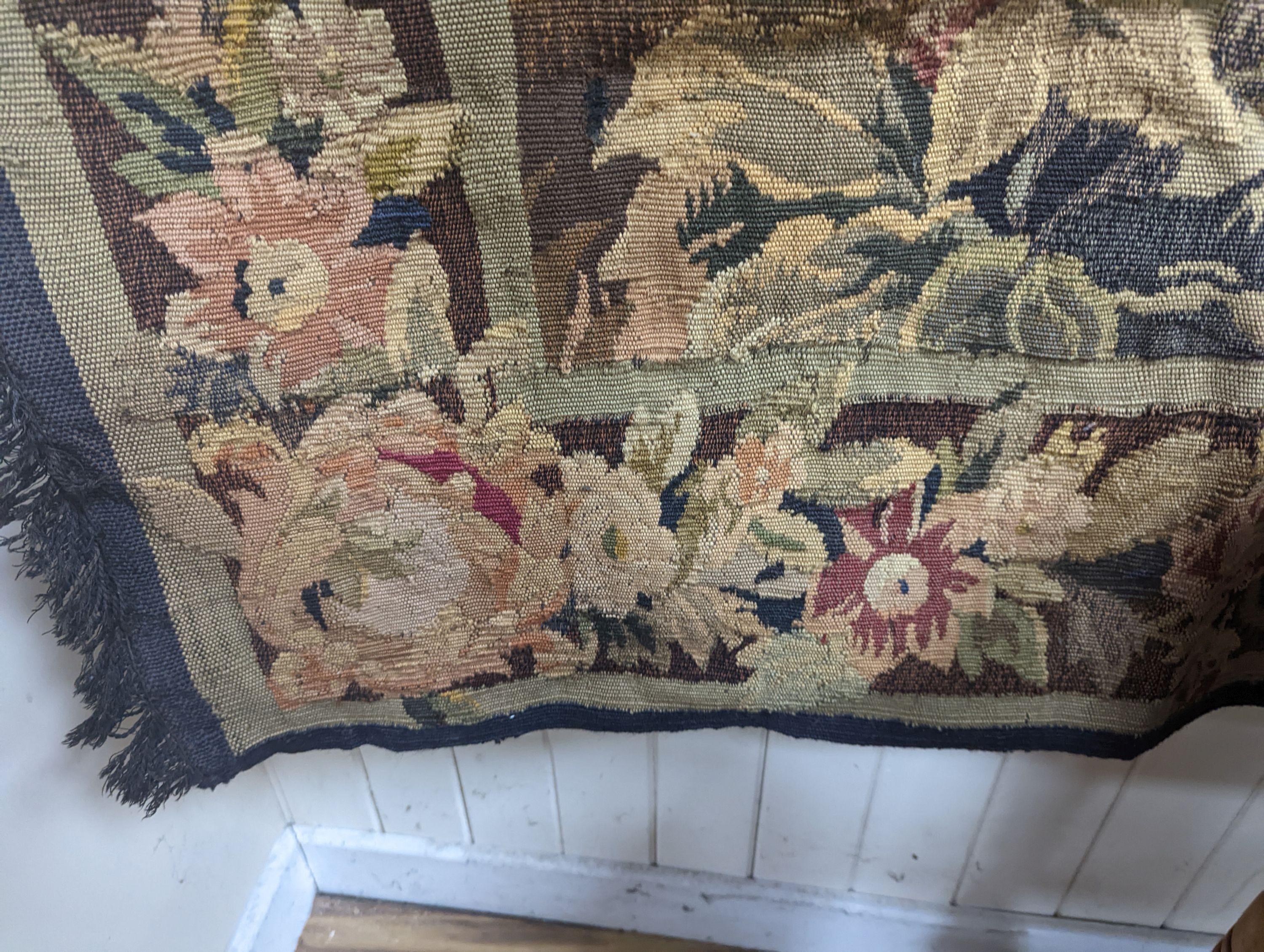 A late 19th / early 20th century French tapestry depicting a woodland scene with trees and flowers with a floral border woven in autumnal colours